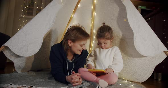 Happy Woman with Her Daughter at Smiling and Talking in Tent  Using Tablet alt