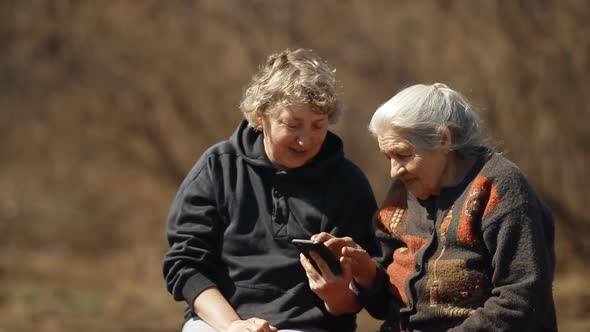 A Woman Teaches Her Old Mother To Use a Smartphone. Portrait of Two Women Looking at Smartphone