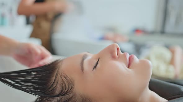 Caucasian young woman lying down and close eye on salon washing bed getting hair washed in salon. alt