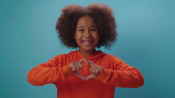 Smiling African American girl making heart shape with fingers looking at camera alt