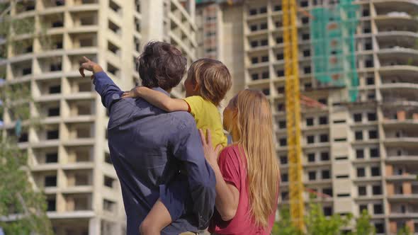 A Family Father Mother and Son Look at a Tall Building That is Under Construction alt
