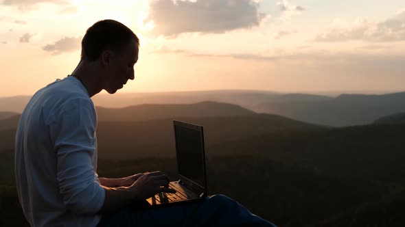 Silhouette of a Man Working on a Laptop Outdoors at Sunset