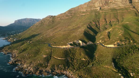 Chapmans Peak road coastline during sunset with table mountain in background, aerial alt