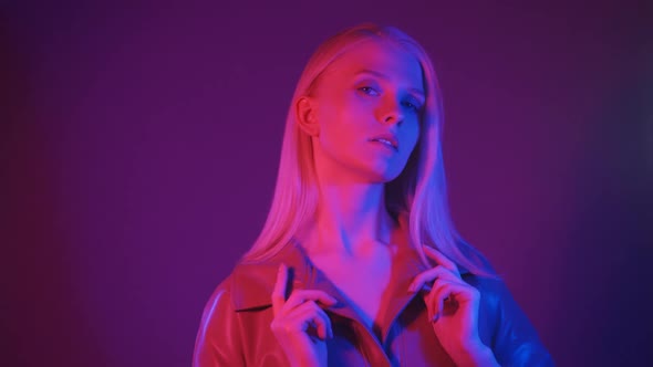 Stylish Blonde Woman in Fashionable Leather Trench Coat Posing in Neon Light