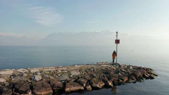 Aerial dolly of woman standing at the edge on stone quay at lake Geneva, Switzerland alt