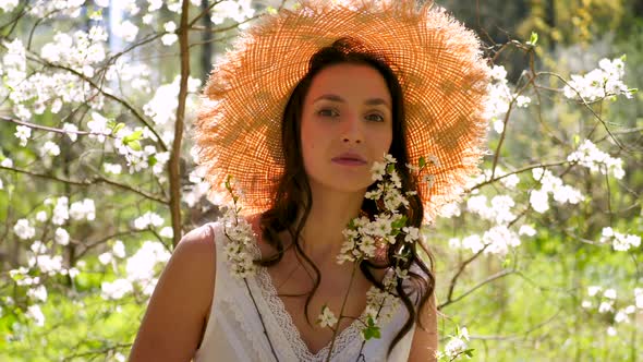 Brunette Woman with Long Hair in a Straw Hat Stands in the Apple Orchard alt
