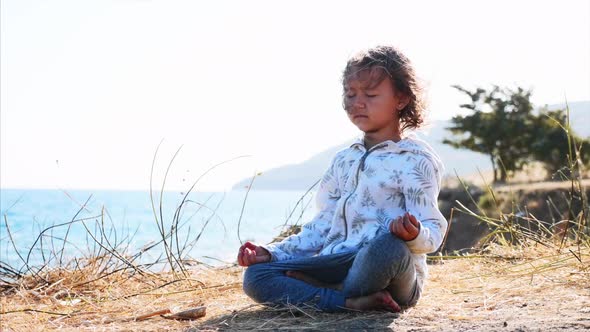 Cute Little Child Gurl Meditating Alone in Lotus Pose at Lake Shore