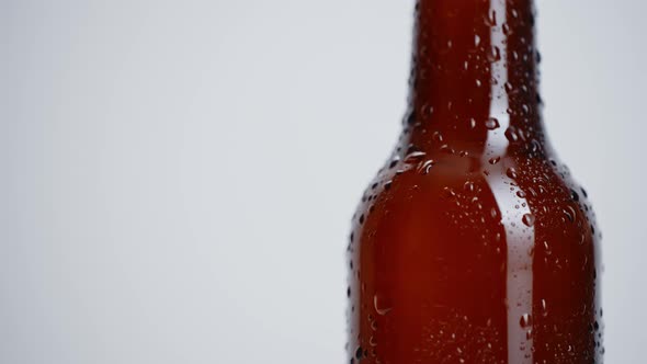 Close-up rotation of beer bottle covered with drops on white background