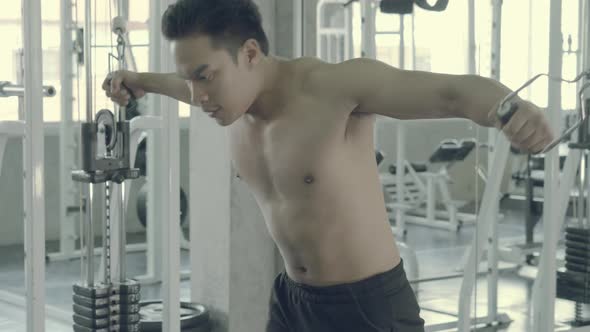 Young asian man doing cable rope triceps pull up exercise for bodybuilding in the gym. alt