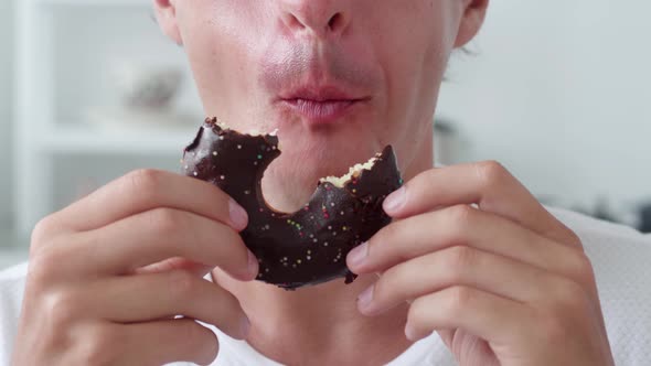 Man Eating Sweet Chocolate Donut Over White Interior Background alt