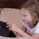 Cute Little Girl Lying on the Sofa Looks at the Screen of the Tablet - VideoHive Item for Sale