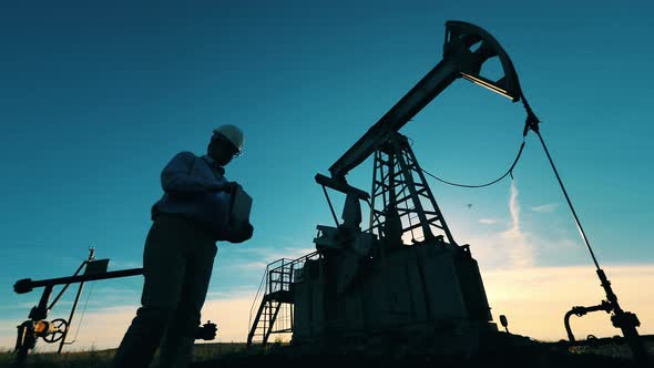 Engineer Working Near Oil Pumpjack and Typing on Laptop alt