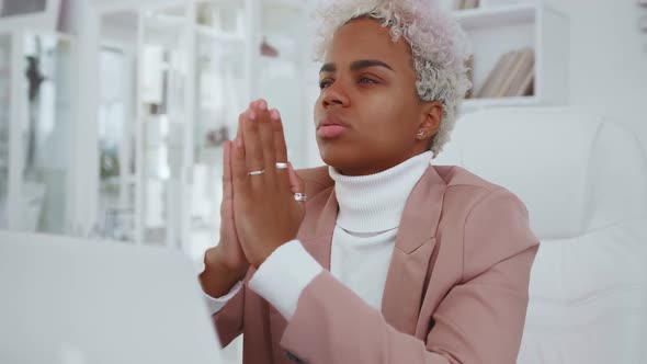Young African American Woman Prays with Palms Folded Sits at Office Desk alt