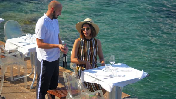 A woman is served wine by a waiter at a restaurant in a luxury resort town in Italy, Europe alt