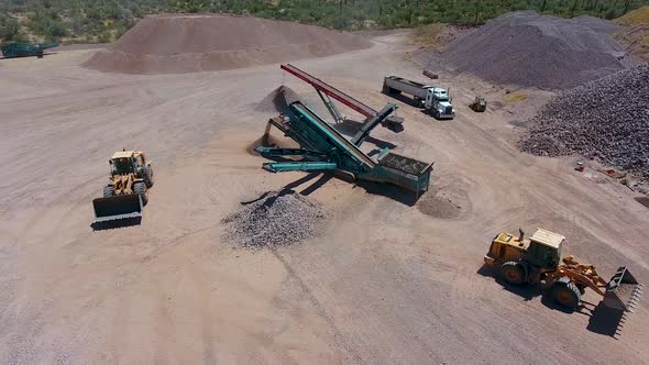 Wide drone shot of an excavators loading rocks on a conveyer belt in a rock quarry alt