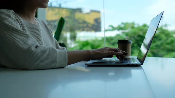 A woman drinking coffee while working and typing on laptop computer