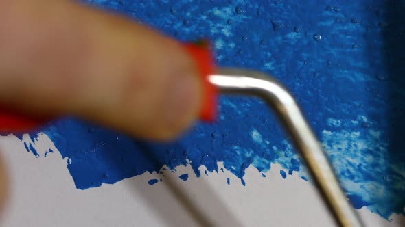 a Hand with a Paint Roller Paints a White Background with Blue Paint