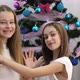 Two Sisters at the Christmas Tree Waving Hello They are Having Fun on New Year&#39;s Eve - VideoHive Item for Sale
