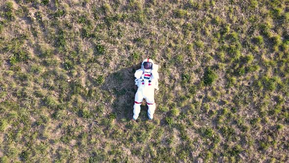 Aerial view of astronaut lying on back on dry grassland