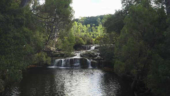 A long small rocky multi-level waterfall in a forest on a sunny day, wide shot alt