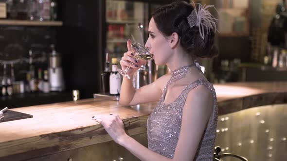 Closeup Portrait of a Young Attractive Woman in a 1920s Style Drink Wine or Champagne at the Bar alt