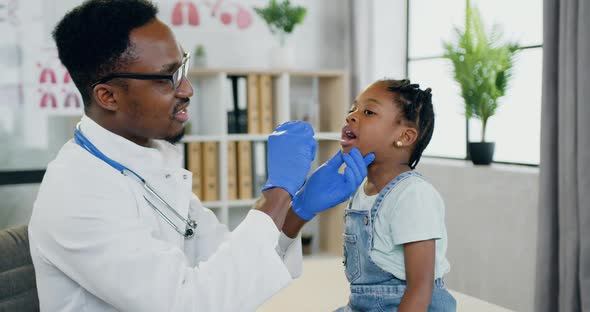 African American Male Doctor which Examining Her throat and Mouth with Spatula alt