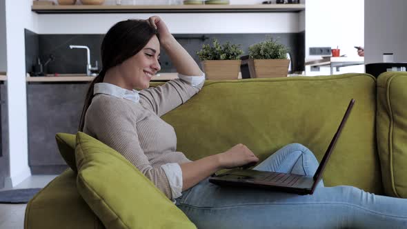 Relaxed Serious Woman Student Using Laptop Device Leaning on Sofa at Home Office, Focused alt