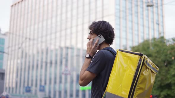 Delivery Man with Backpack Calling to a Client on the City Street alt