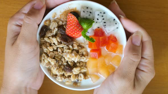 Woman Hands Rotate Bowl of Homemade Granola with Yogurt Raisins Fresh Berries alt