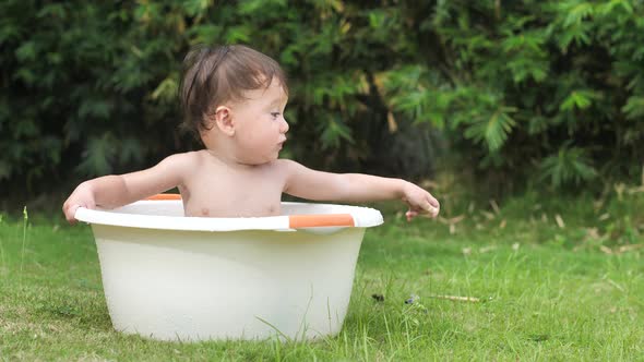 A Funny Cute Child Feels Great Sitting in a Basin on a Green Lawn