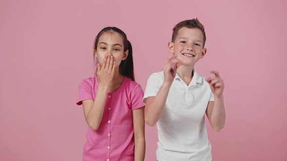 Cute Positive Brother and Sister Posing to Camera Girl Sending Blow Kiss Boy Pointing Fingers Pink alt