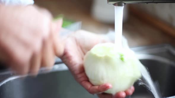 Woman washing fennel bulb under running water alt