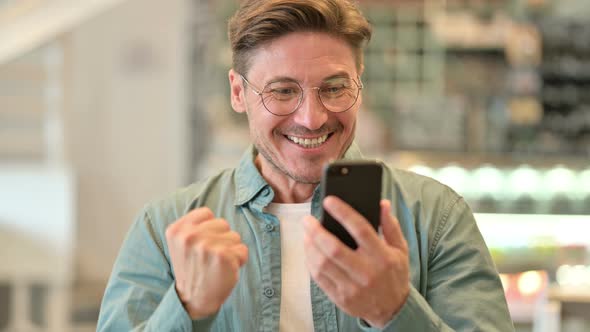 Portrait of Excited Middle Aged Man Celebrating Success on Smartphone  alt