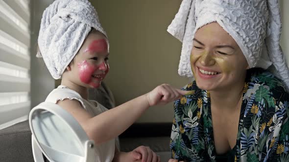 Little Girl with a Cosmetic Mask on Her Face Helps Her Mother To Make a Cosmetic Mask alt
