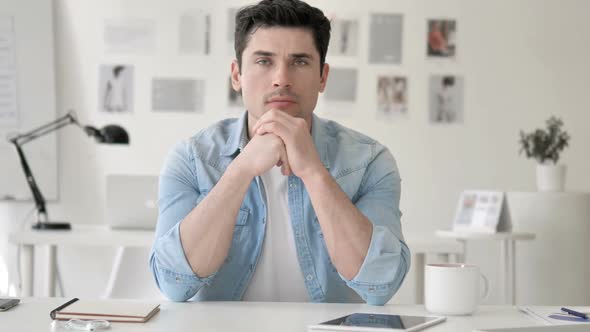 Confident Casual Young Man Sitting at Workplace alt
