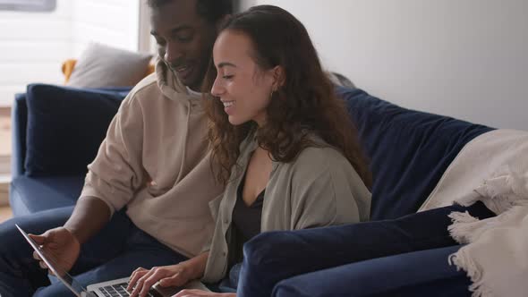 Relaxed Young Couple At Home Sitting On Sofa Browsing Internet On Laptop Computer