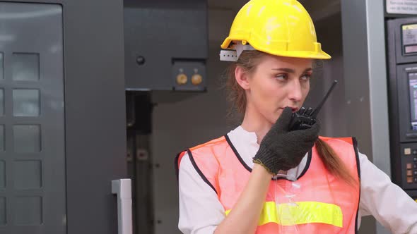Serious female engineer worker calling and talking to colleague with walkie talkie