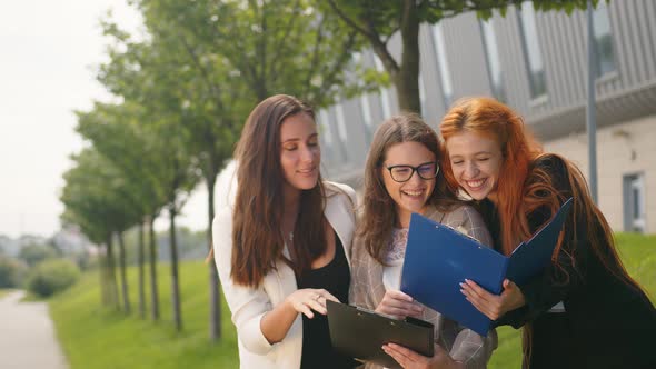 Business Women Browse the Contents of Documents in a Black Folder and Have Fun Laughing. Cheerful alt