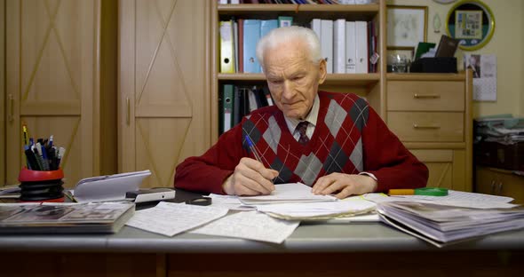 Senior Businessman Writing on Paper at Table in Office alt