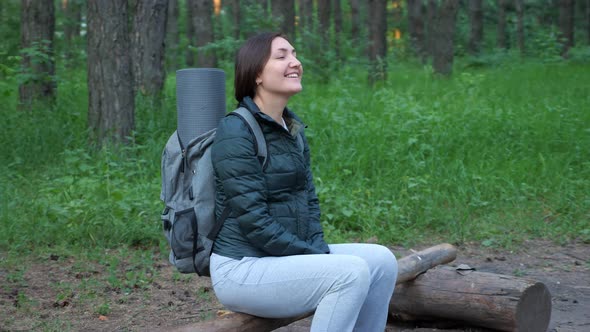 Happy Woman with Backpack Sitting on a Log in the Forest