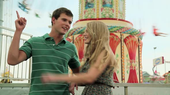 Teenage couple at fun fair, girl dragging boyfriend away alt