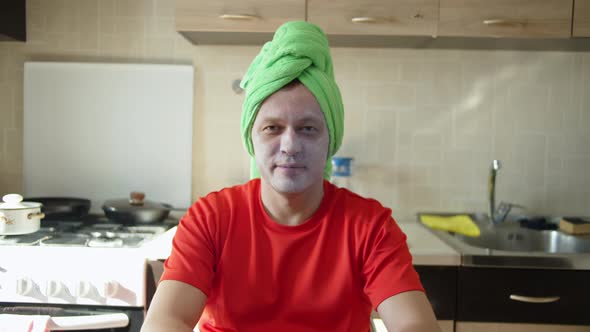 Man sitting with a cosmetic mask on his face and a towel on his head, home care alt