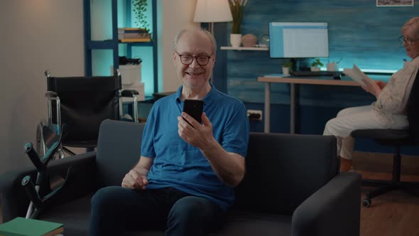 Retired Man Holding Smartphone to Chat on Video Call with Family alt