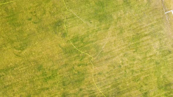 Top down aerial view of football field surface covered with green grass and sprinklers spraying alt
