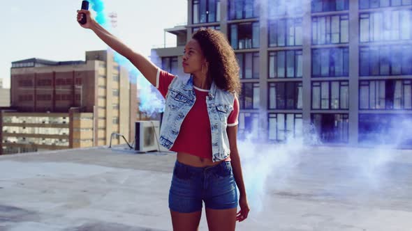 Fashionable young woman on urban rooftop using a smoke grenade alt
