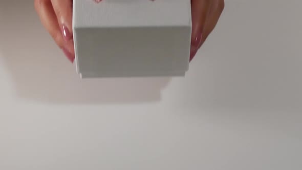 hands of young woman give a white box with a pastel pink bow as a gift alt