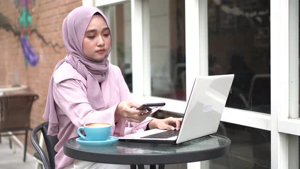 happy Asia hijab woman using smart phone and calling,  drink coffee while sitting at cafe