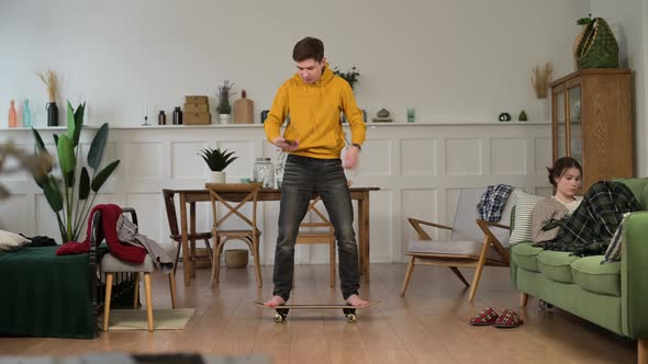 A young guy fooling around at home and learning to stand on a skateboard, then falling alt