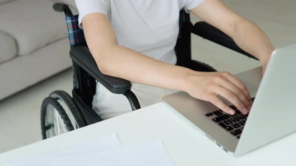 Female Student Learning Online Using Laptop Typing Sitting in Wheelchair in Apartment Busy with alt