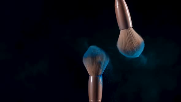 Makeup Brushes Touch Each Other and Particles of Blue Crushed Paint Fly Into Space Against a Black alt